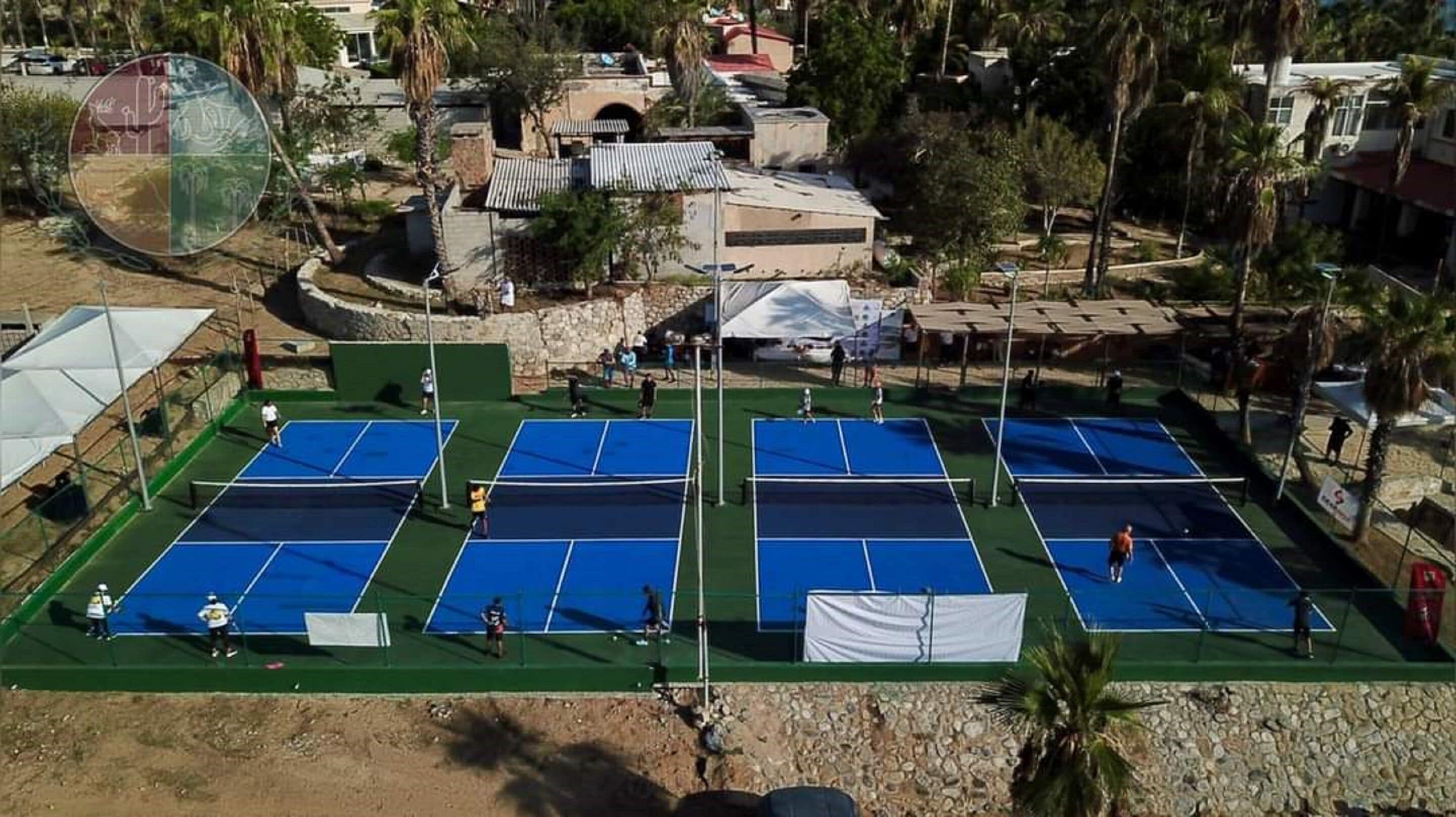 A tennis court complex with multiple courts, surrounded by palm trees and residential buildings.