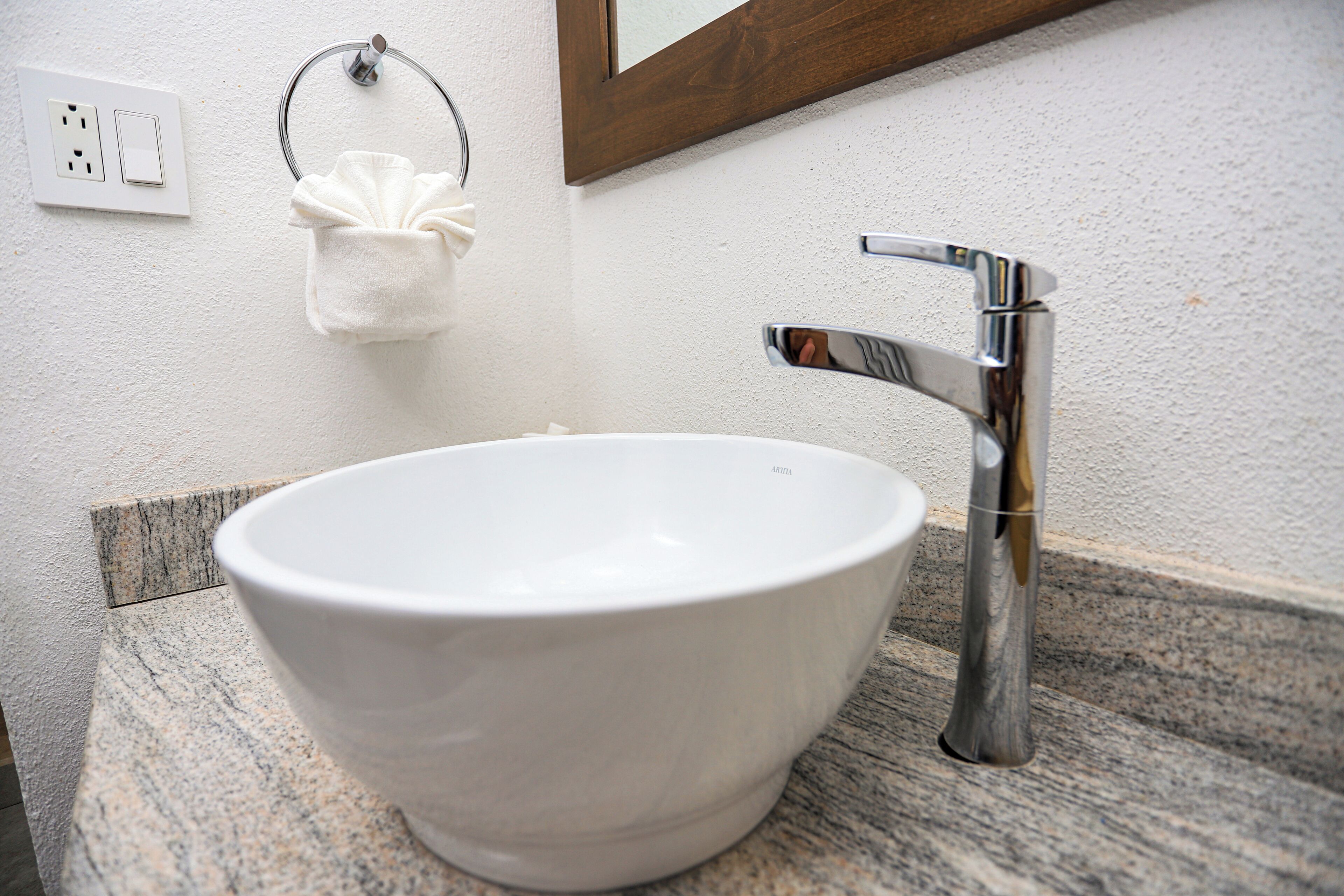 A white ceramic sink with a modern chrome faucet, a towel ring with a white towel, and a power outlet on the wall.