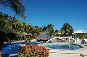 A pool area with multiple pools, palm trees, and a thatched-roof structure. - Buena Vista Oceanfront & Hot Springs Resort (Buenavista)