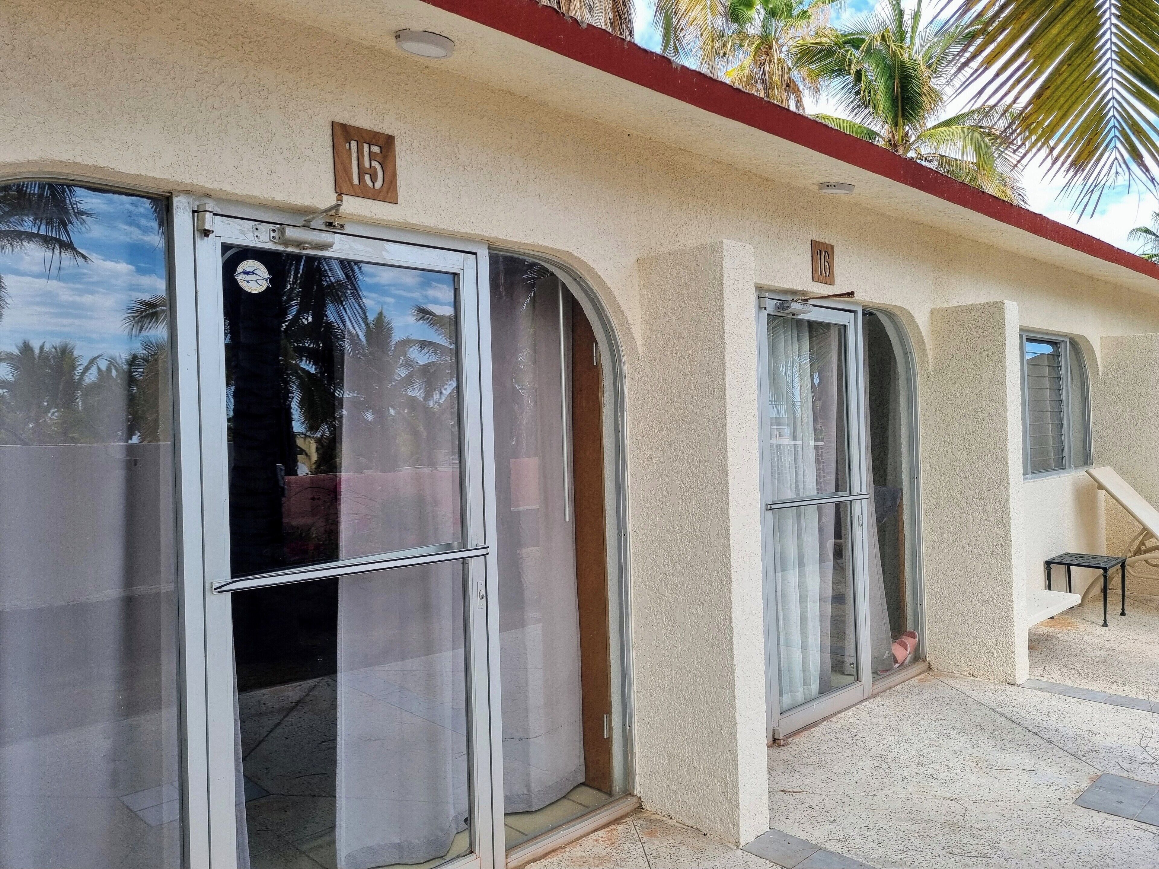 A building with two doors marked with numbers 15 and 16, a staircase, and a view of palm trees.
