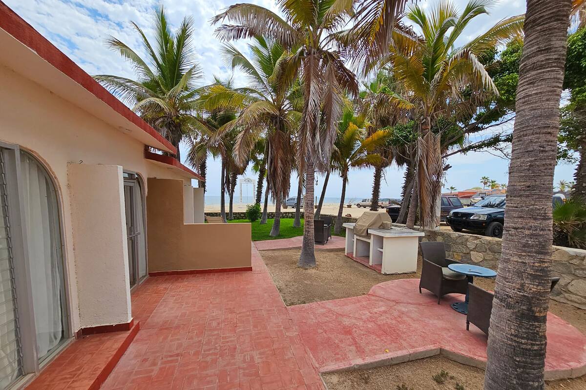 A hotel patio with a red brick floor, outdoor seating, palm trees, and a view of the beach.