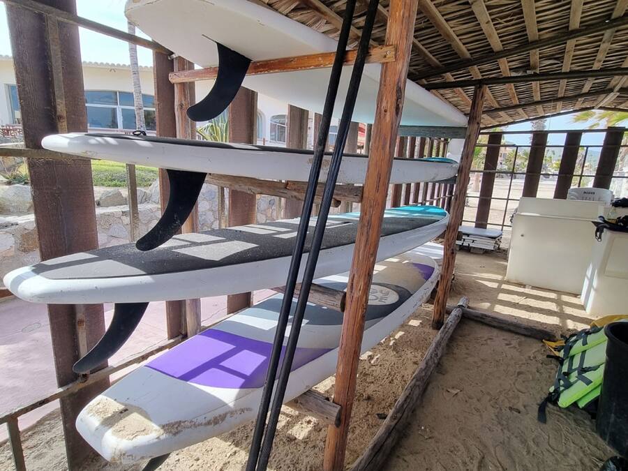 Zona techada con varias tablas de surf y palas colgadas en estantes de madera.