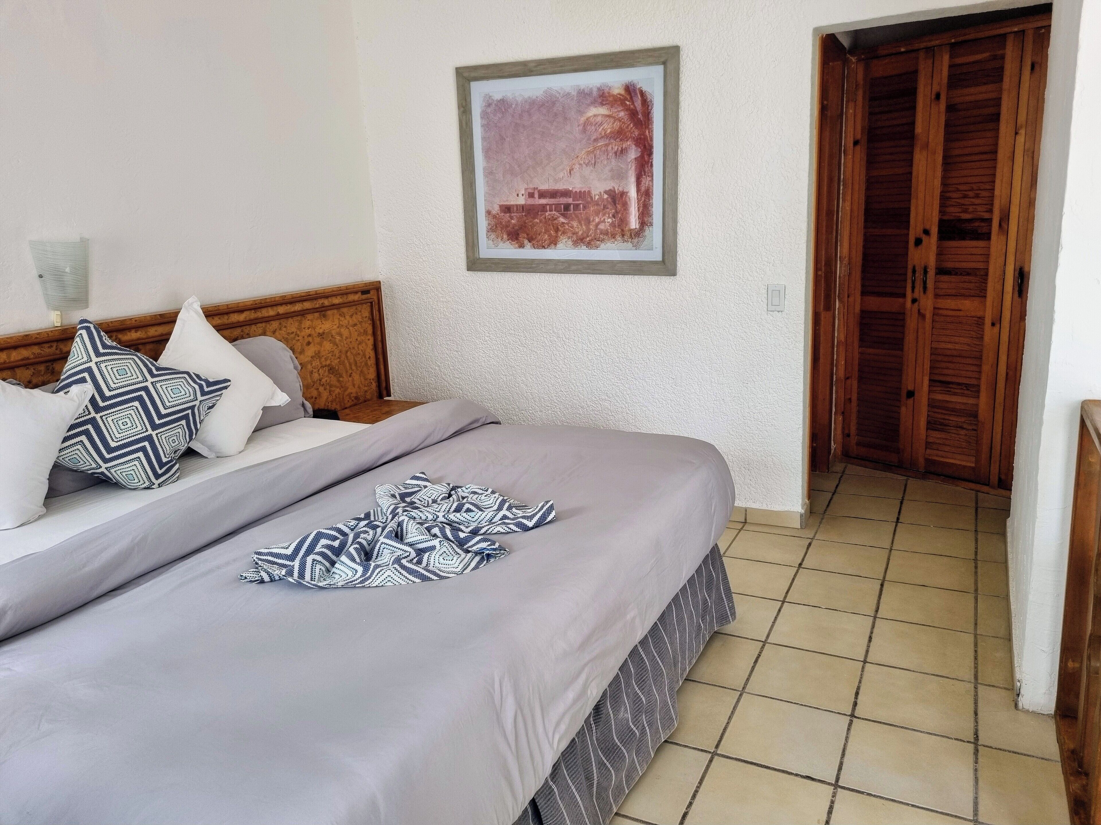 Un dormitorio con una cama, almohadas, una colcha, un cuadro enmarcado en la pared y una puerta de madera.