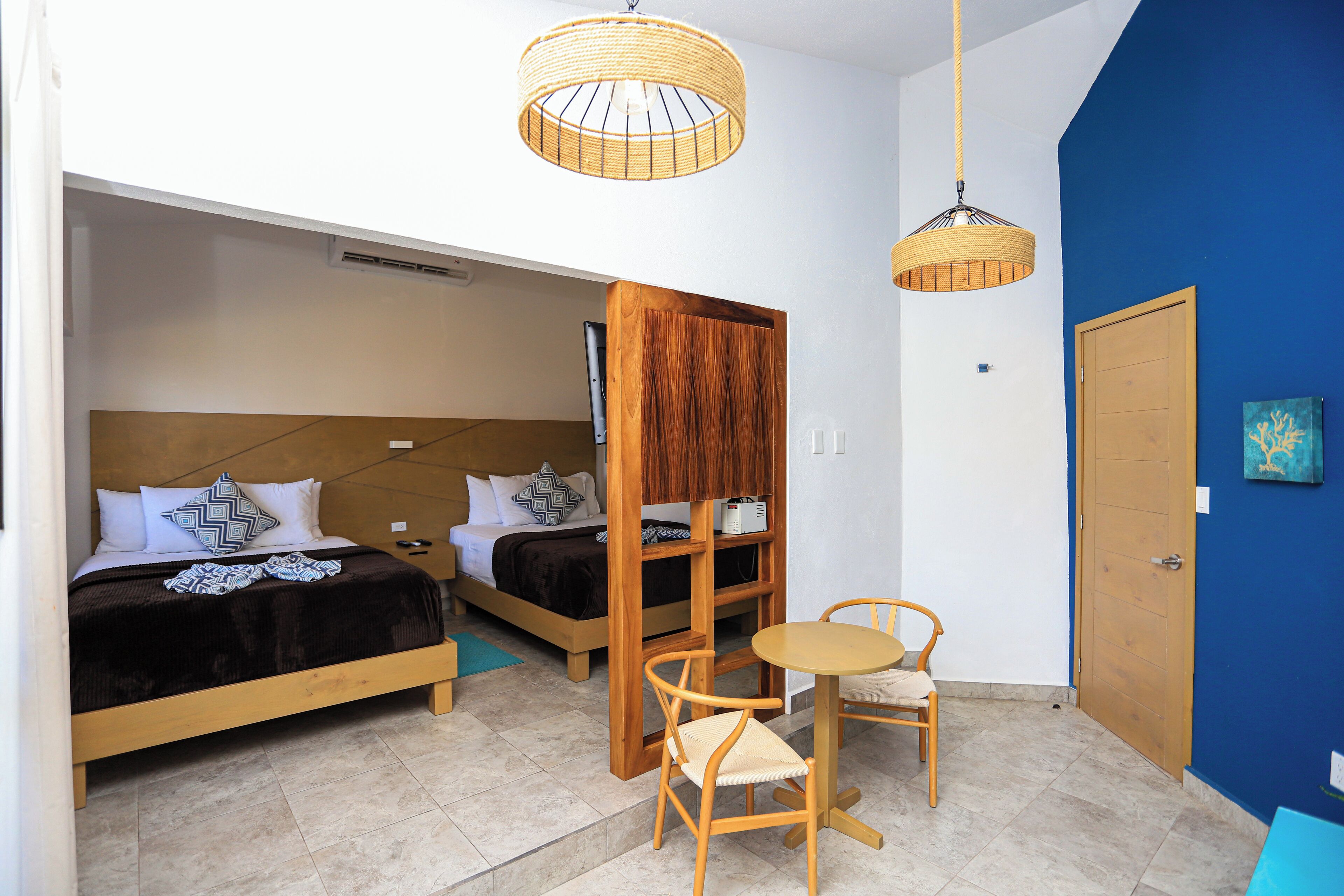 Une chambre avec deux lits, une armoire en bois, une petite table avec des chaises et deux lampes suspendues.