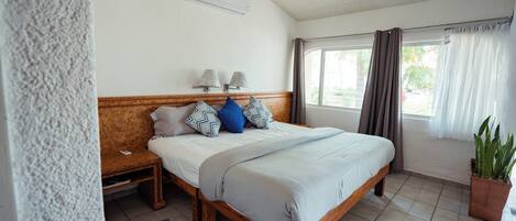 Una habitación de hotel con una cama de madera, una mesita de noche, una planta en maceta y una ventana con cortinas.