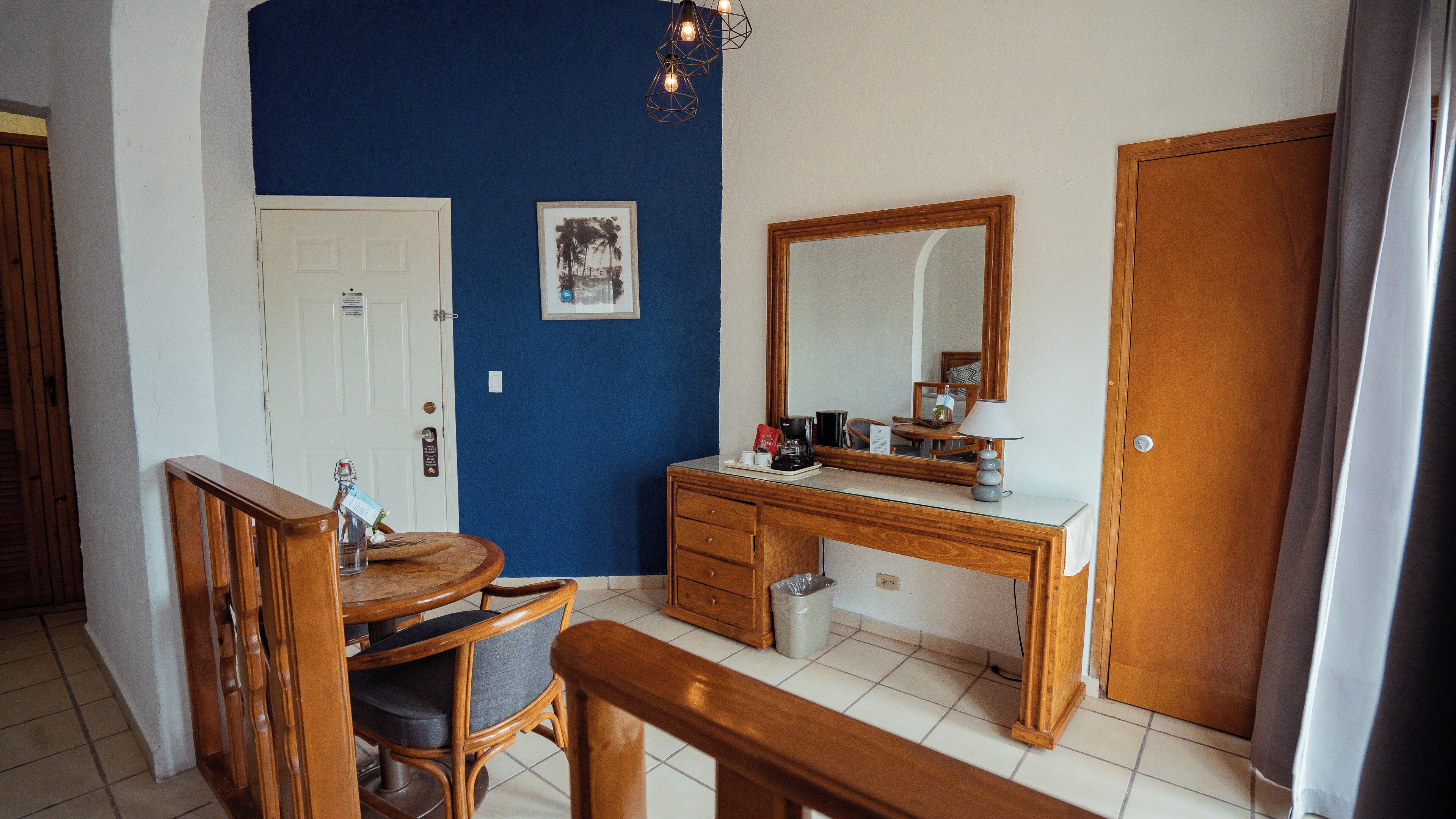 A room with a wooden desk, a chair, a small dining table, a mirror, and a door.