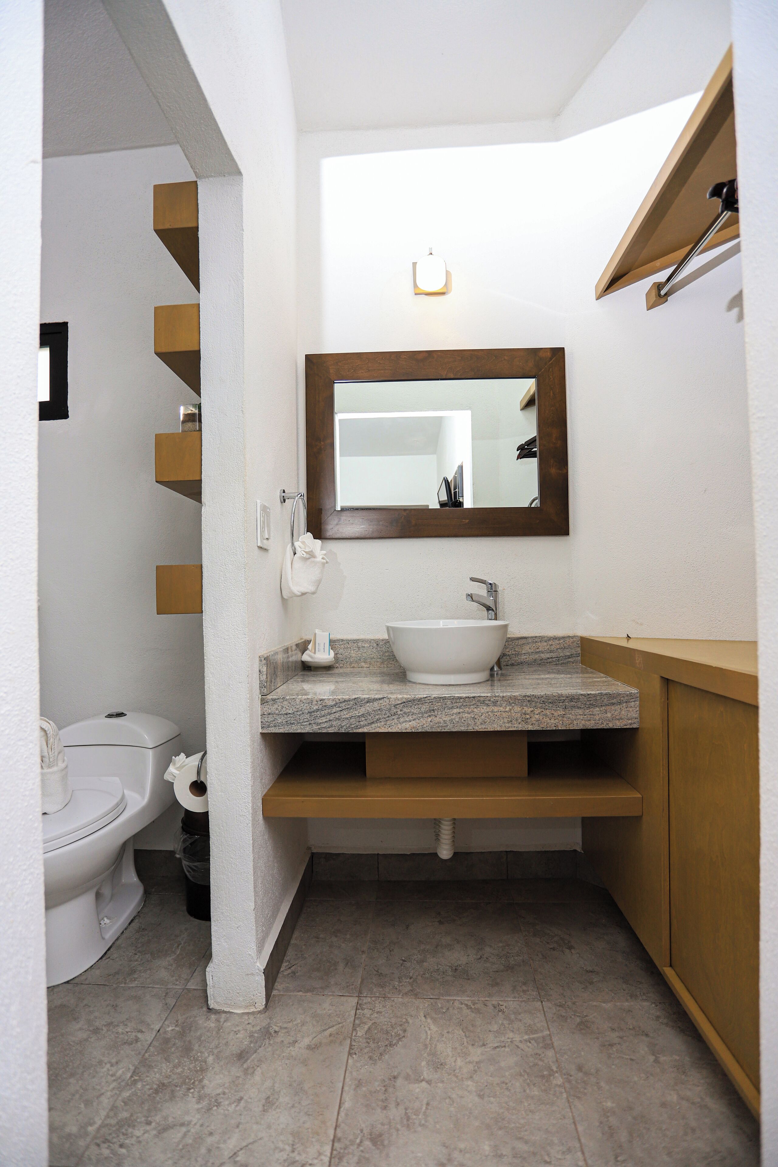 Un baño con inodoro blanco, lavamanos con encimera de mármol, tocador de madera y espejo sobre el lavamanos.