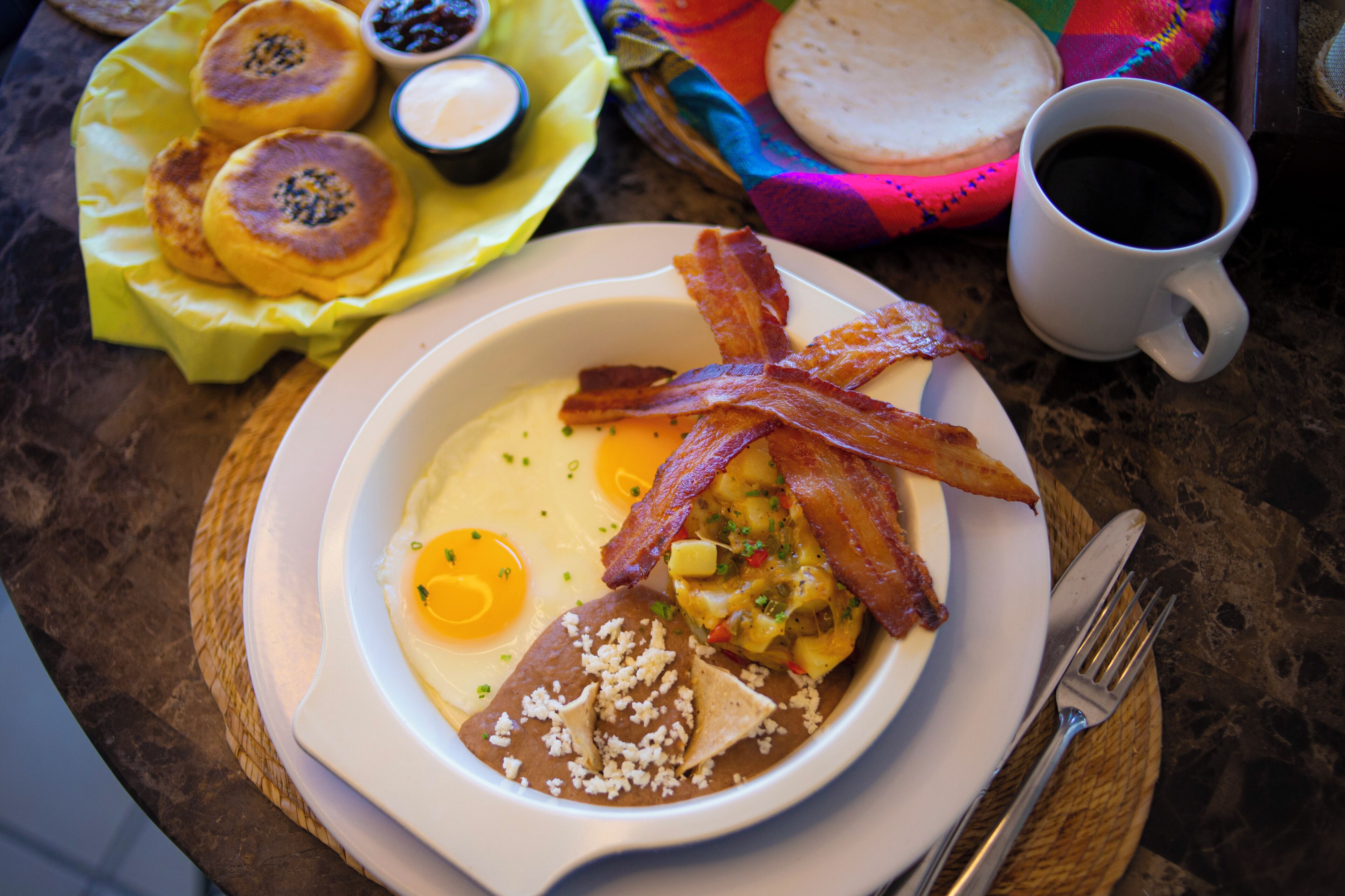 A breakfast plate with eggs, bacon, and refried beans.