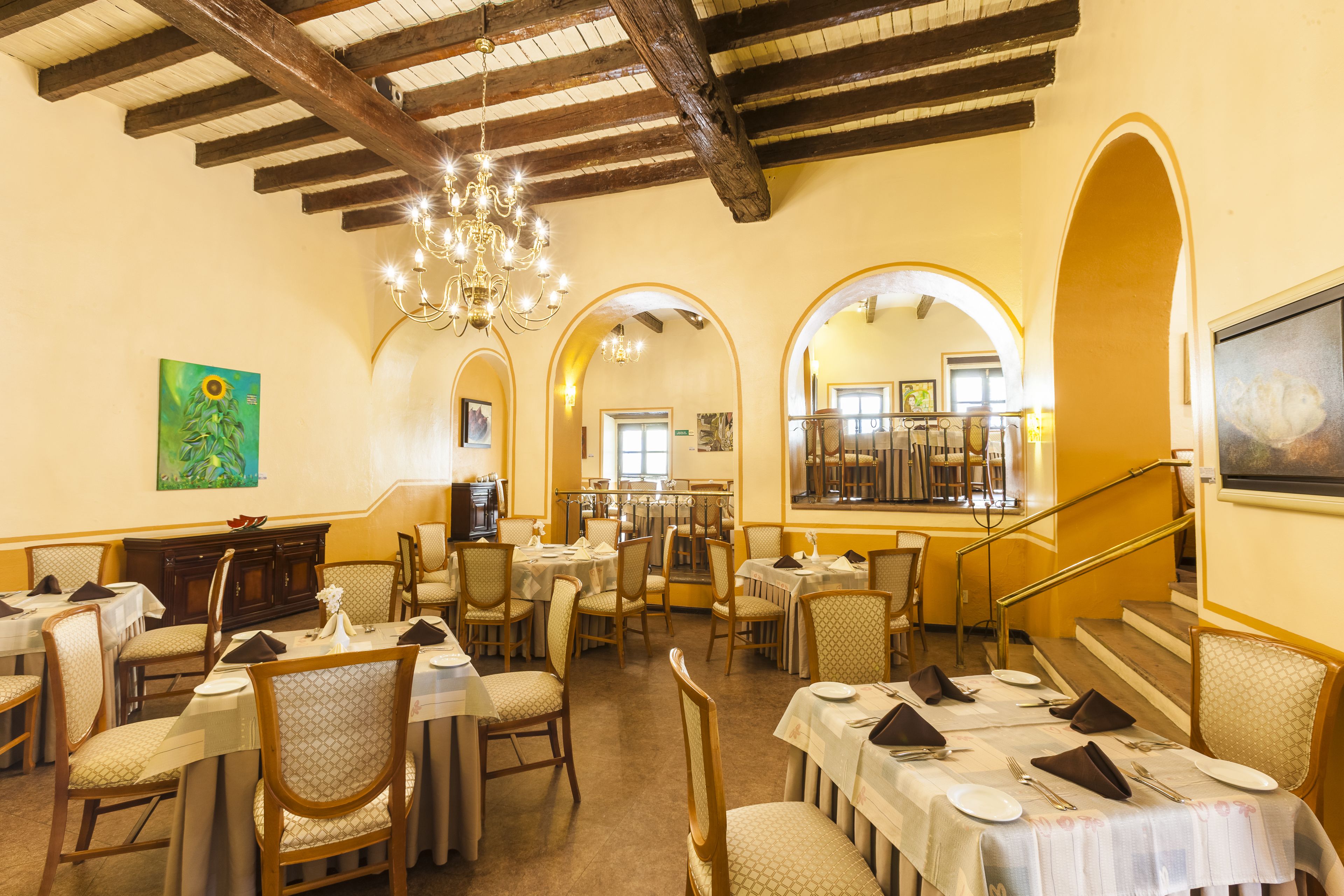 Un espace repas avec des tables dressées pour le service, des poutres en bois au plafond et un lustre.