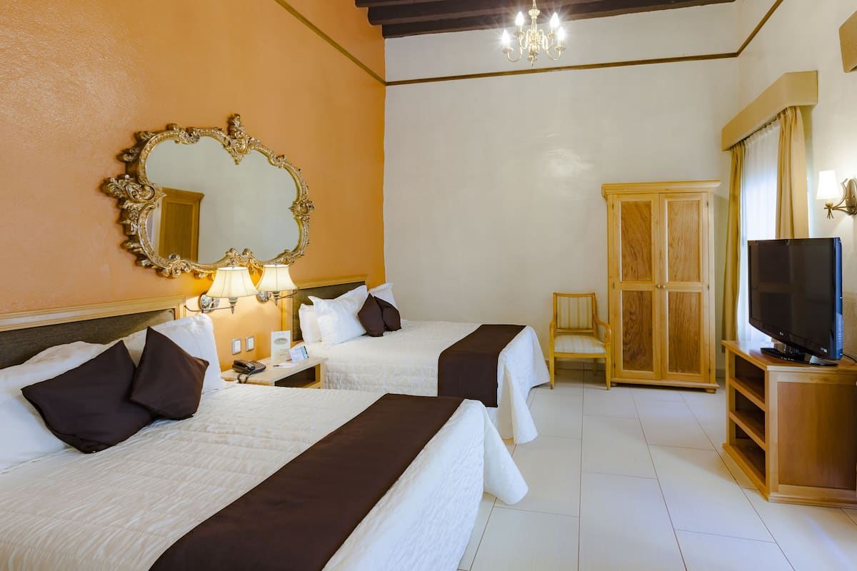 Une chambre d’hôtel avec deux lits, un grand miroir, une télévision et une armoire en bois.