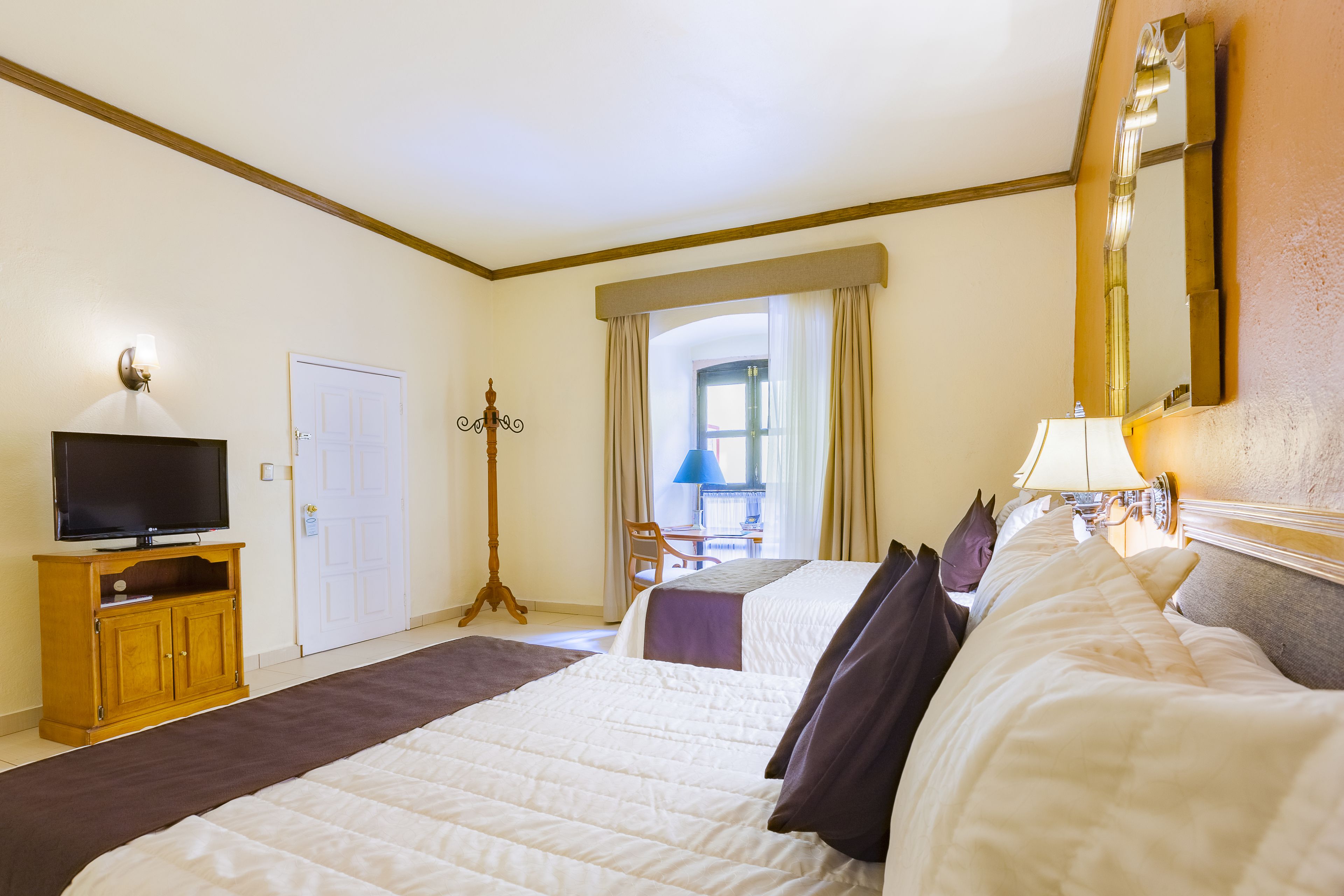 Une chambre d’hôtel avec deux lits, une télévision, un bureau et une fenêtre avec des rideaux.
