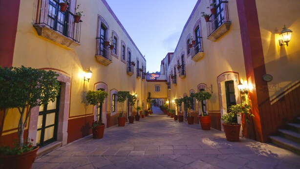 A narrow alleyway with buildings on either side, potted plants, and a staircase leading to an upper level. - Hotel Mesón de Jobito (Zacatecas)