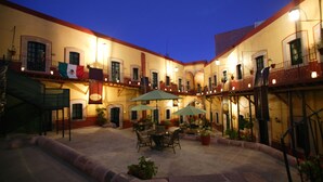 A courtyard with outdoor seating, potted plants, and a flag. - Hotel Mesón de Jobito (Zacatecas)