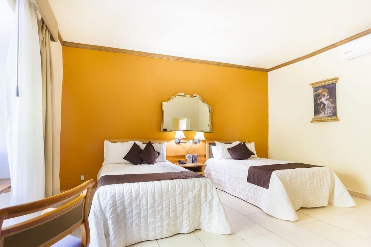 Une chambre d’hôtel avec deux lits, une tête de lit en bois, un miroir, une table de chevet et un tableau au mur.