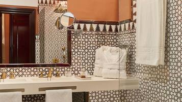 Un baño con baldosas estampadas, un espejo grande, un perchero y un lavamanos con toalla.
