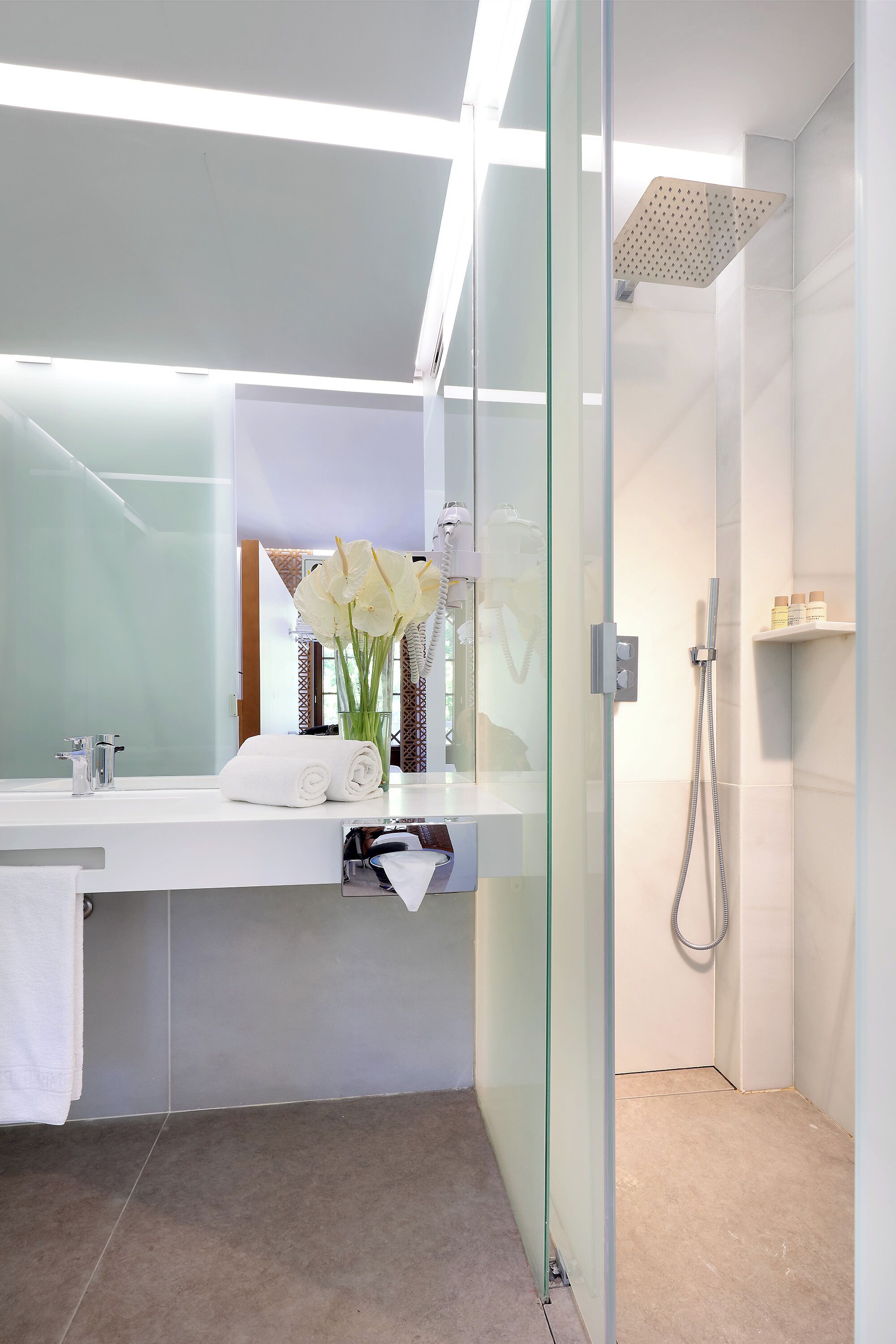 A modern bathroom with a glass shower enclosure, a white vanity with a mirror, and a vase of white flowers.