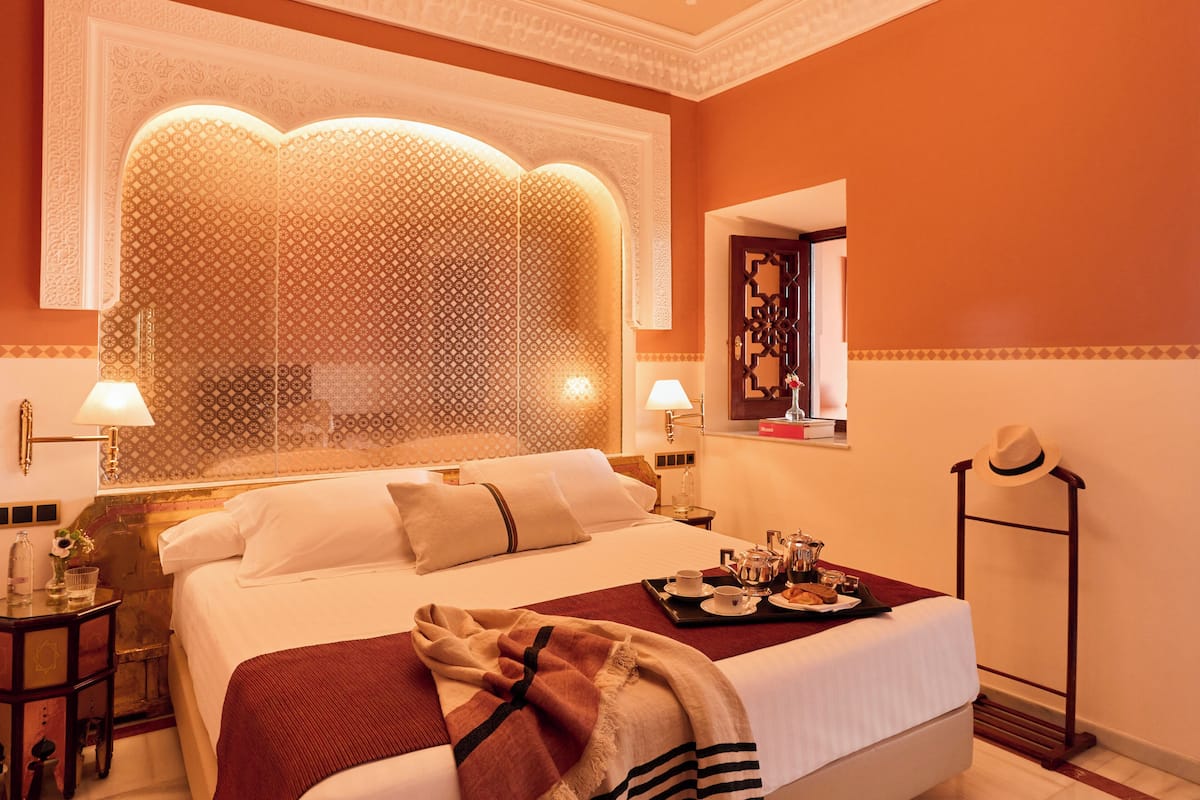 Une chambre d’hôtel avec un grand lit, deux tables de chevet, une commode, un miroir, un panneau décoratif mural et un plateau avec des articles pour le petit-déjeuner.