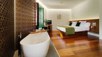 Una habitación de hotel moderna con una bañera grande, una cama con ropa de cama blanca, un escritorio con una computadora y una puerta verde.