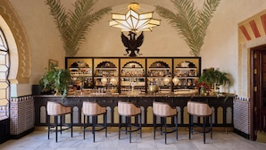 A bar area with a decorative ceiling, a bar counter, and several stools. - Hotel Alhambra Palace (Granada)