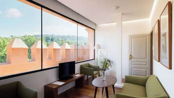 Een moderne woonkamer met een groot raam, een flatscreen televisie, een ronde tafel en twee groene banken.