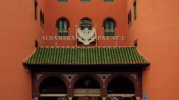 Un edificio anaranjado grande con una cúpula central y varios balcones. La entrada tiene una alfombra roja y un letrero que dice "ALHAMBRA PALACE".