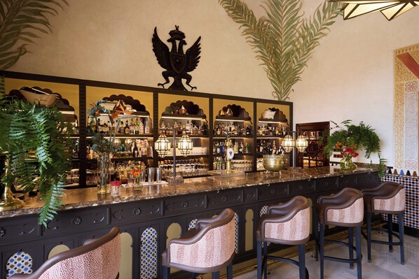 A bar with a decorative emblem, multiple liquor bottles, and bar stools. - Hotel Alhambra Palace (Granada)