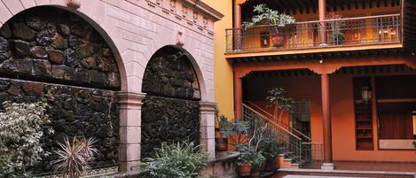 A courtyard with a stone wall, potted plants, and a tiled floor.