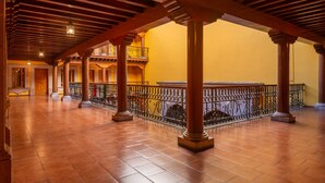 Interior espaçoso com pisos de azulejo, colunas de madeira e uma varanda com grades de metal.