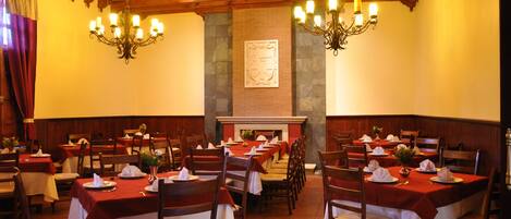 Un restaurante con varias mesas dispuestas para comer, vigas de madera en el techo y candelabros sujetos a la pared.