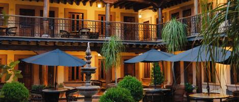A courtyard with a fountain, potted plants, outdoor seating, and a building with balconies.
