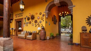 Interior de restaurante com parede amarela, mobiliário de vime e chão de azulejos.