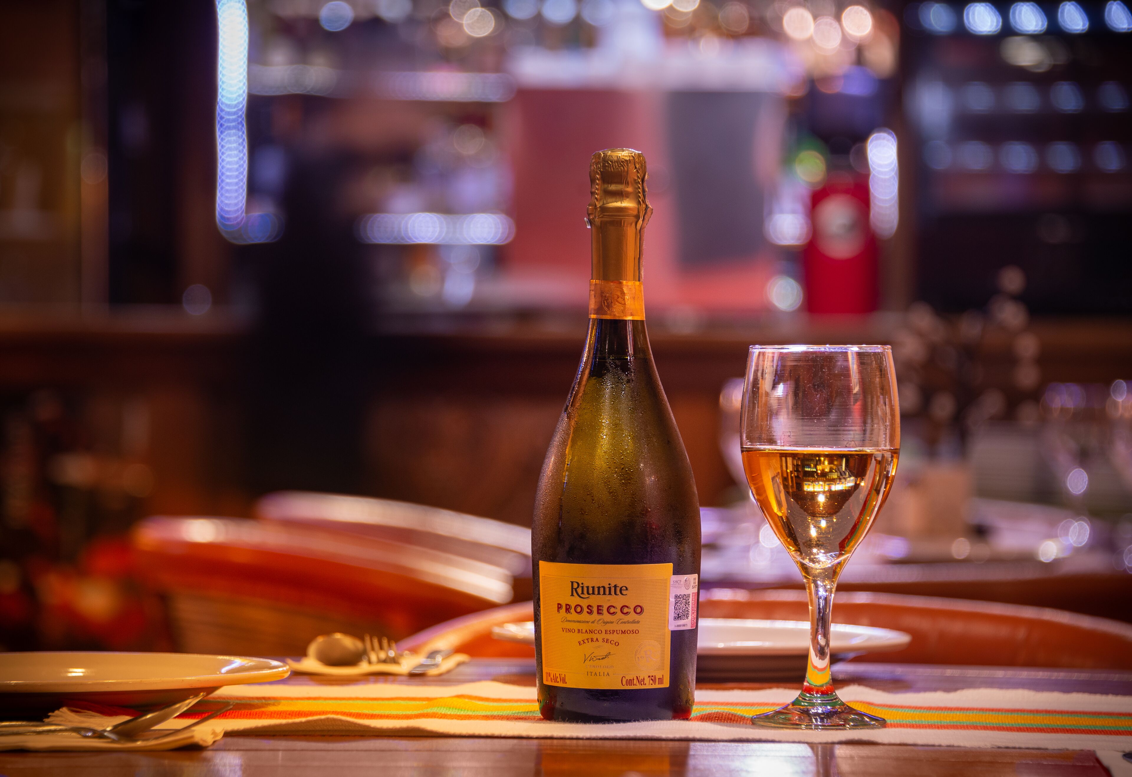 A bottle of Riunite Prosecco and a wine glass on a table with a colorful placemat.