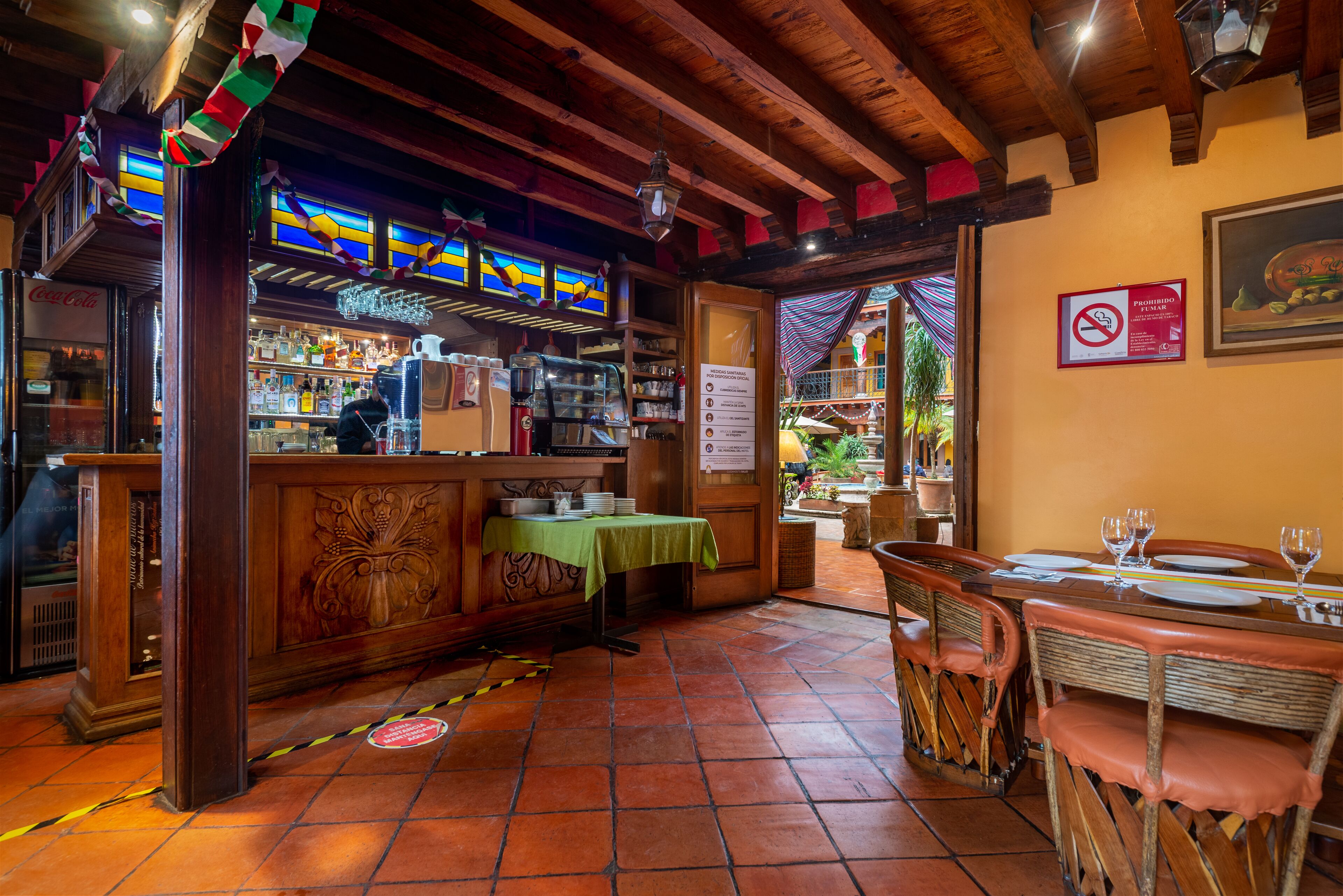 Un interior de restaurante con vigas de madera, una zona de bar y una sección de comedor con sillas y mesas.