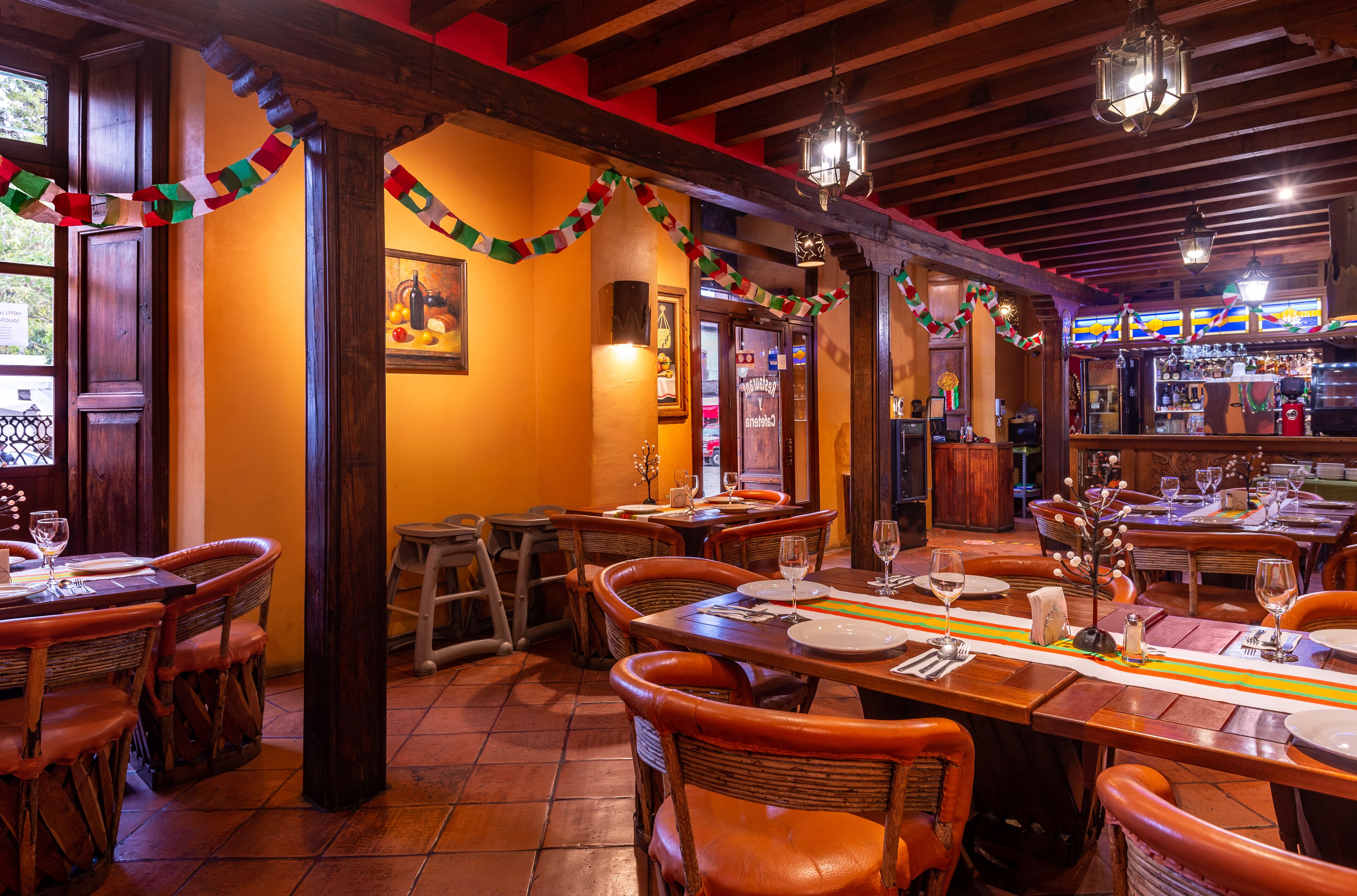 Un restaurante con mesas y sillas de madera, una zona de bar y decoración festiva.