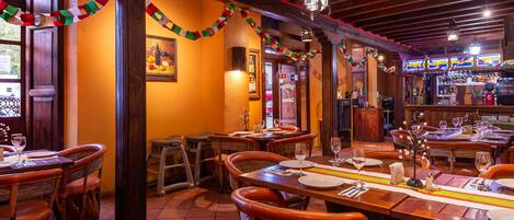 Un restaurante con mesas y sillas de madera, una zona de bar y decoración festiva.