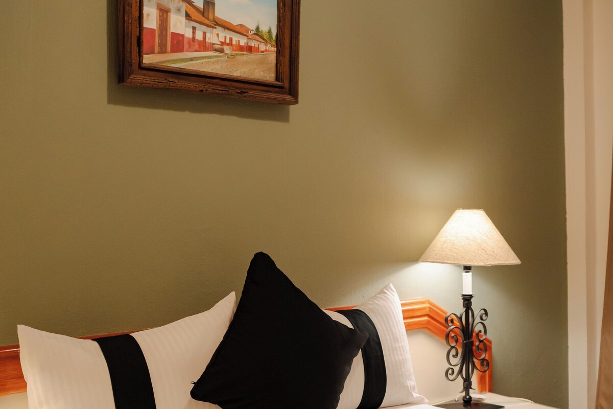 Ein Hotelzimmer mit einem Bett, Kissen, einer Lampe und einem Bild an der Wand.