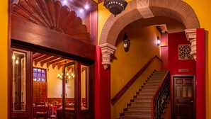 Um saguão de hotel com uma escadaria, uma área de refeições e um balcão de recepção.