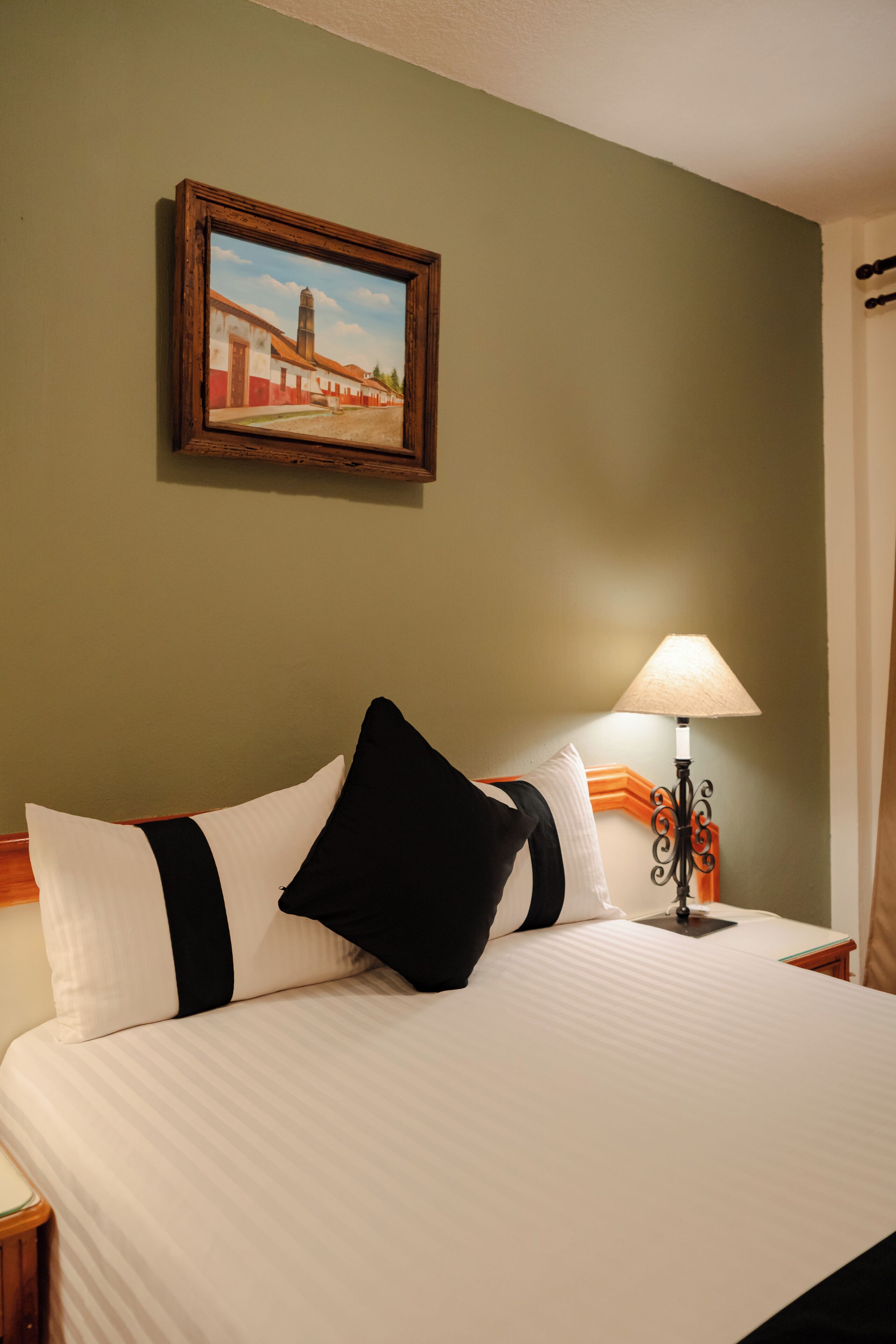 Une chambre d’hôtel avec un lit, des oreillers, une lampe et un tableau au mur.