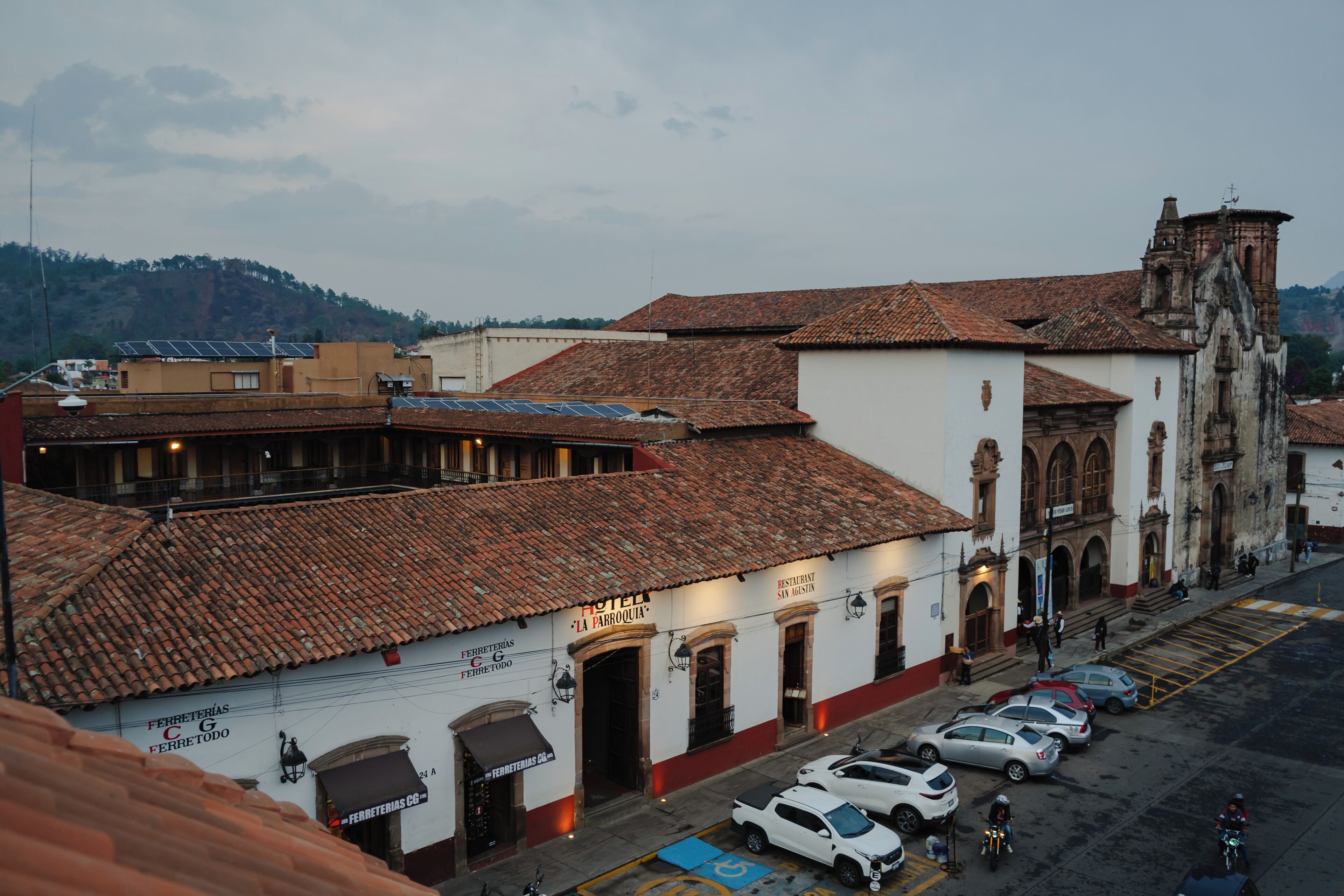 A hotel with a tiled roof, a bell tower, and parked cars on the street.
