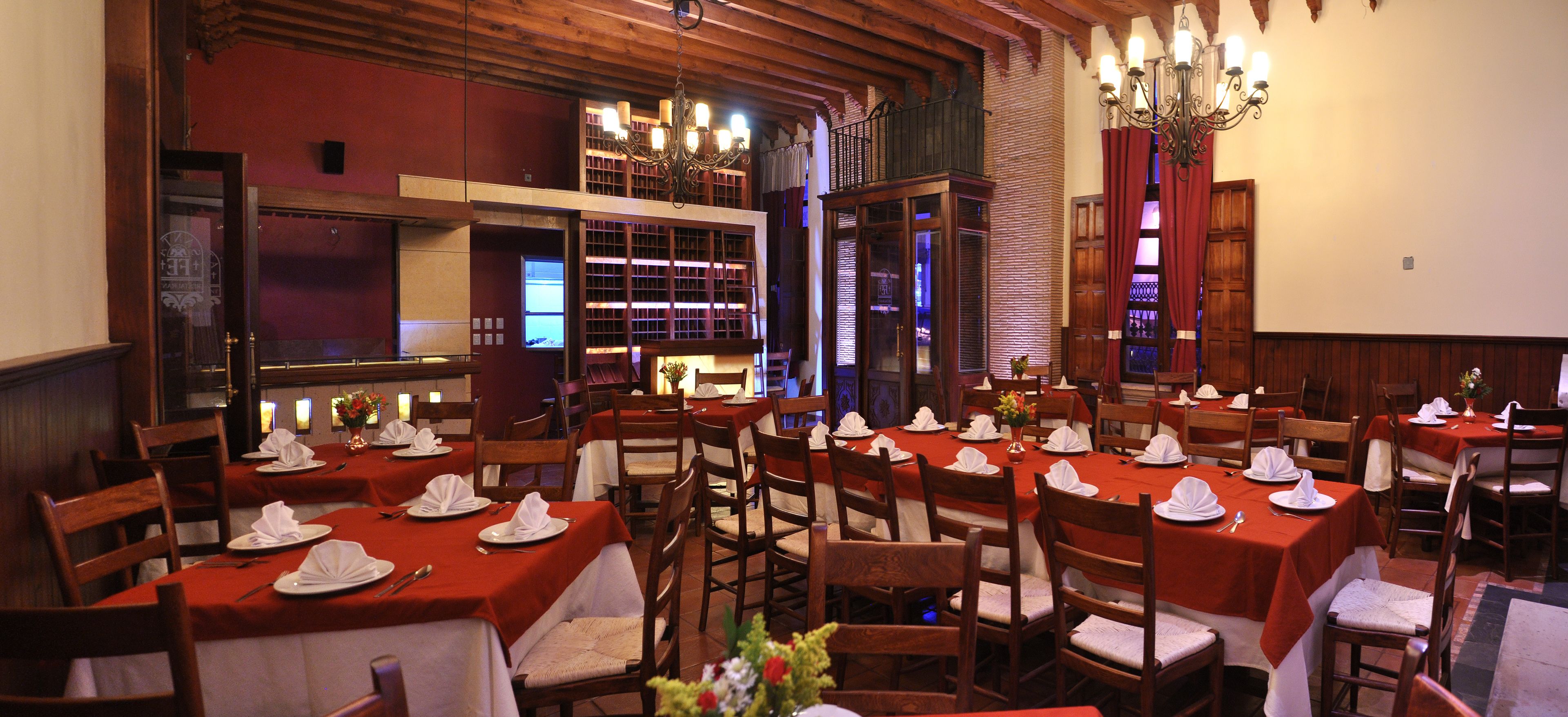 A restaurant with multiple tables set for dining, wooden chairs, and a chandelier.