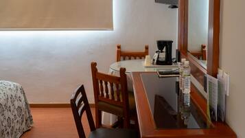 A hotel room with a bed, a desk with a chair, a coffee maker, a bottle of water, a flat-screen TV mounted on the wall, and a window.