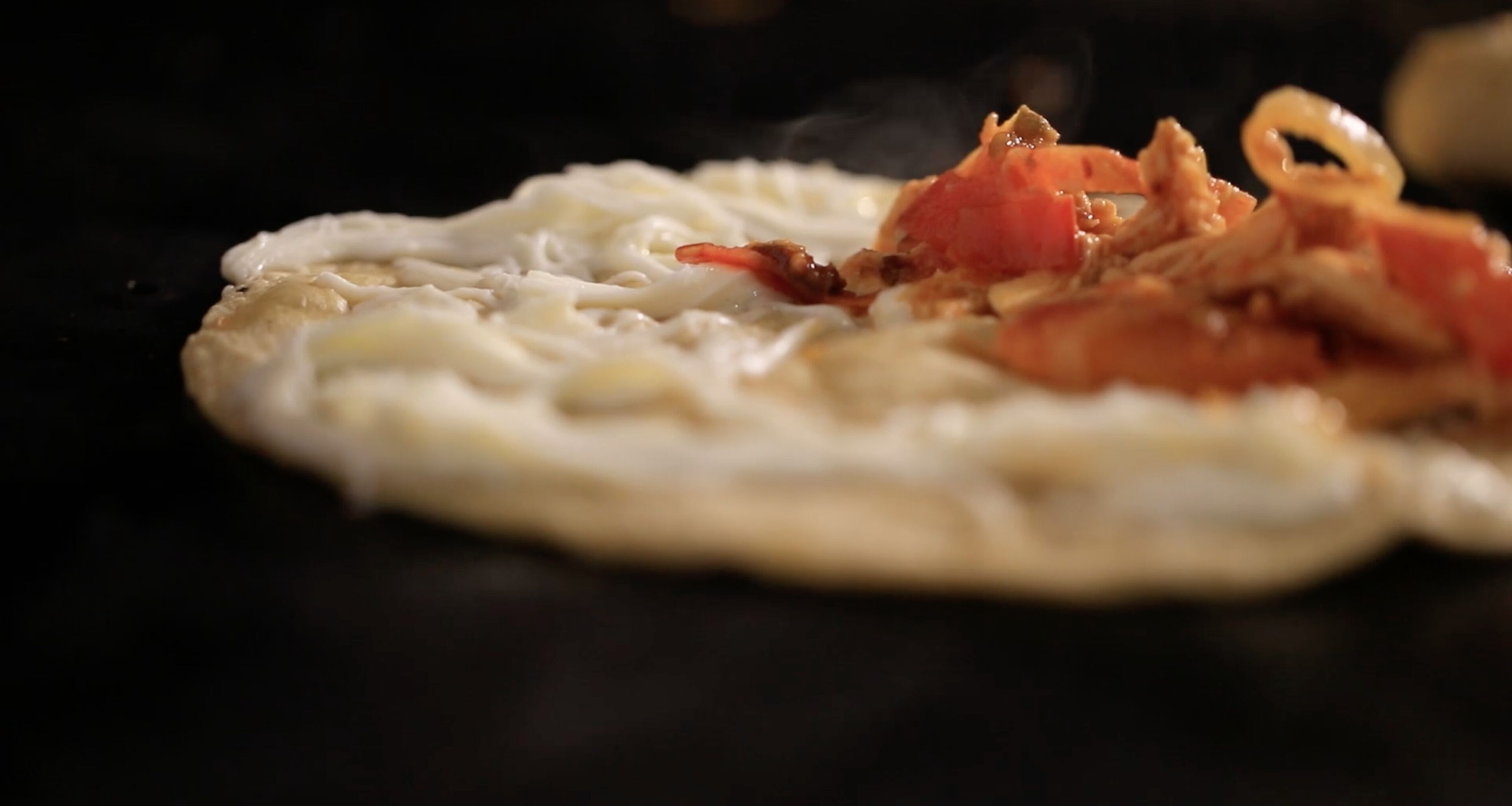 A flatbread with toppings on a dark surface.