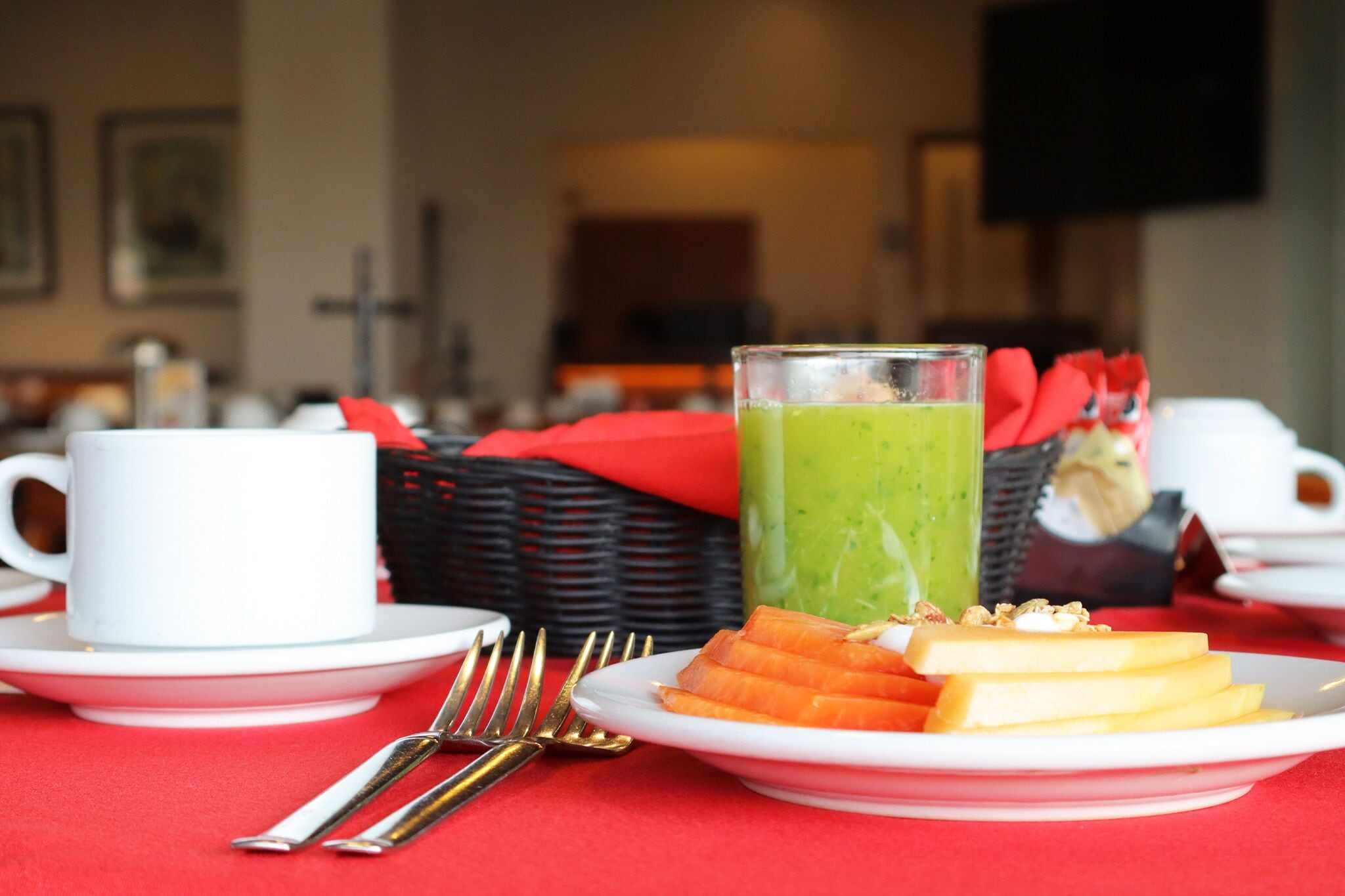 Desayuno con un batido verde, salmón y pan sobre un mantel rojo.
