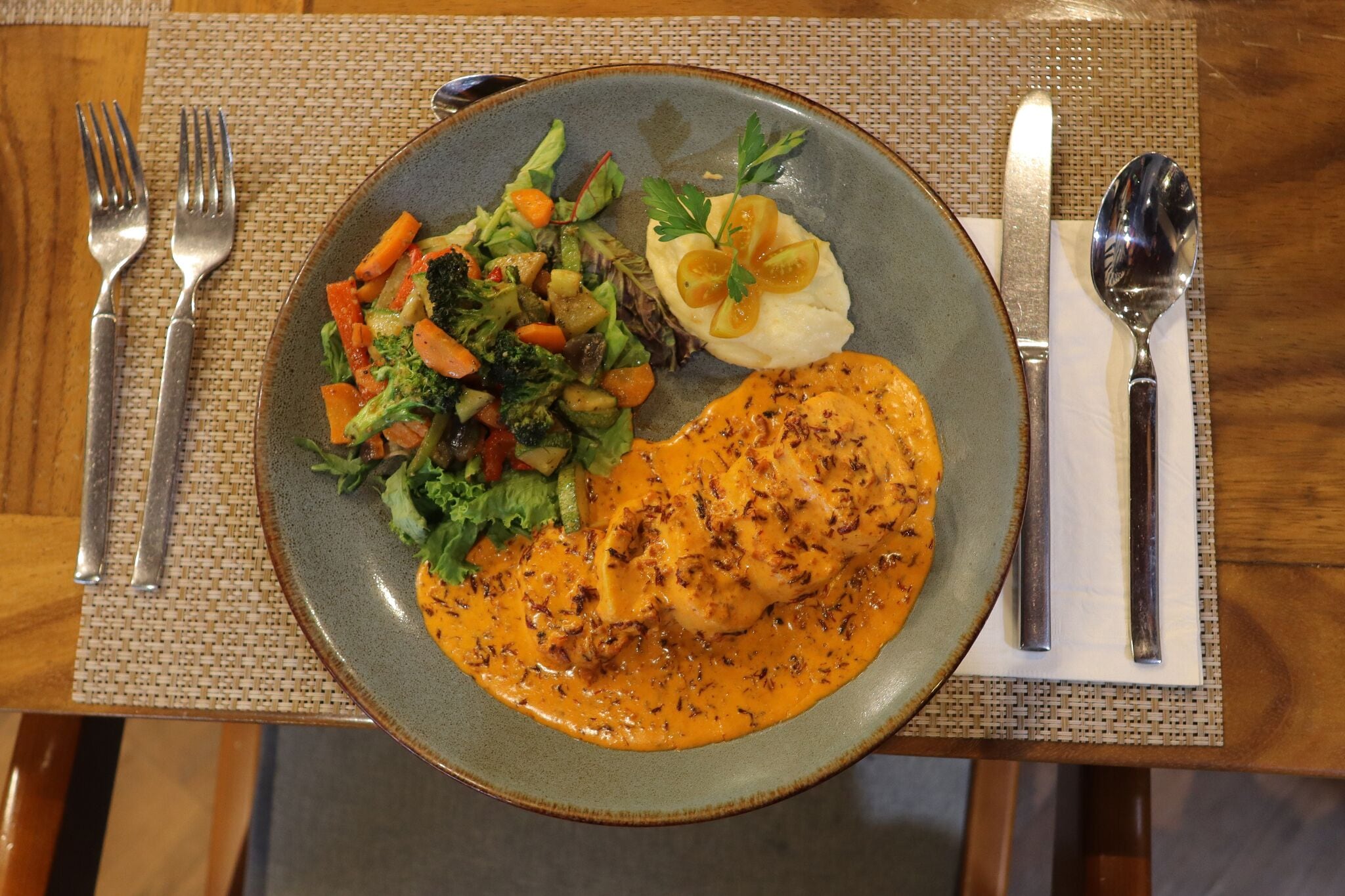 A plate of food with a salad, mashed potatoes, and a chicken breast with sauce.
