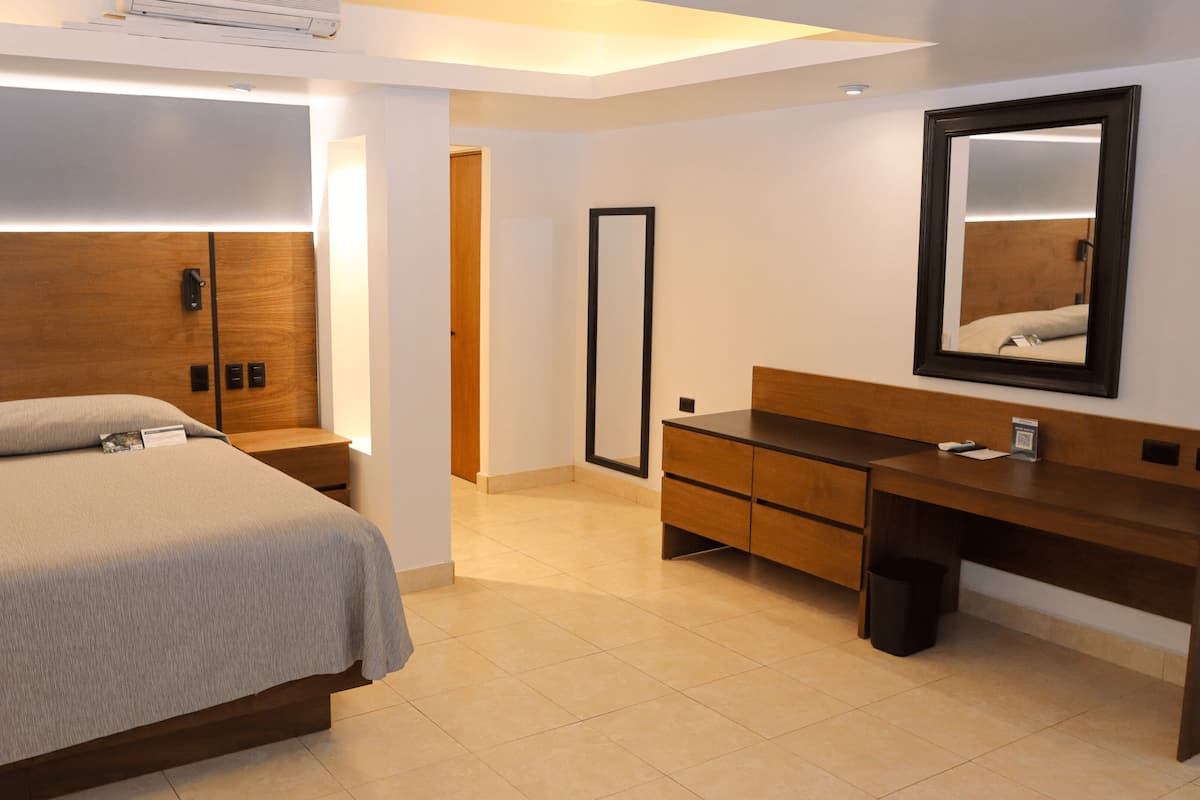 Une chambre d’hôtel moderne, équipée d’un lit, d’une table de chevet, d’une commode en bois et d’un grand miroir.