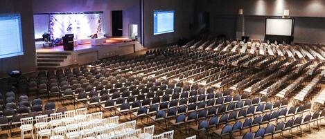 Een vergaderzaal met rijen stoelen, een podium en een groot scherm.