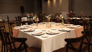 Un salón de banquetes con mesas redondas, sillas y centros de mesa florales.