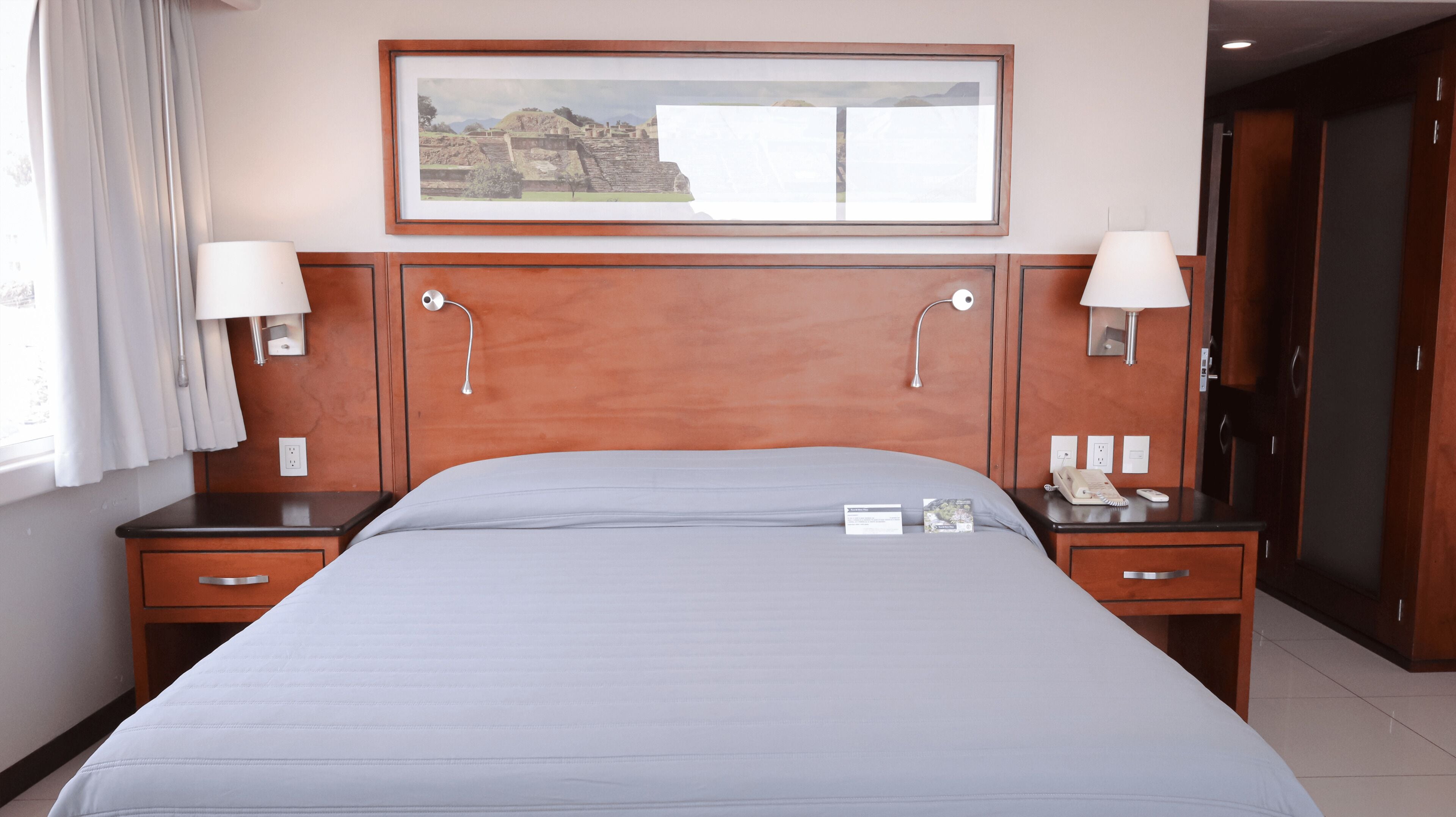 A hotel room with a large bed, two bedside tables with lamps, a framed picture on the wall, and a door to the right.