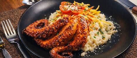 A plate of grilled octopus with a side of rice and vegetables.