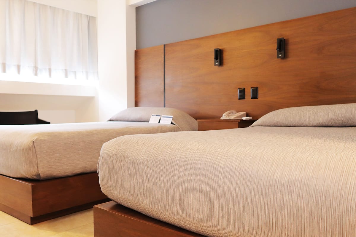 Une chambre d’hôtel avec deux lits, une tête de lit en bois, des tables de chevet et une fenêtre avec des rideaux.